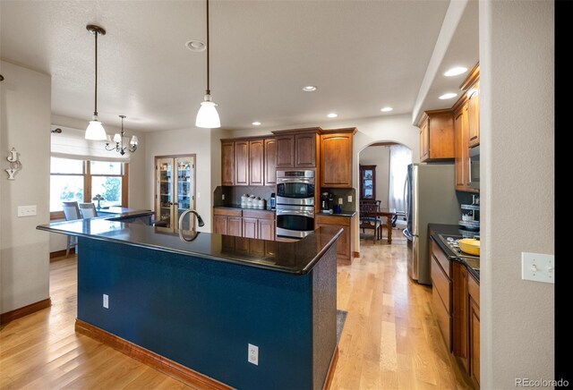 kitchen with appliances with stainless steel finishes, hanging light fixtures, light hardwood / wood-style floors, an inviting chandelier, and a kitchen island with sink