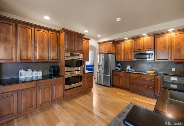 10215 W Wesley Dr, Lakewood, CO 80227 - kitchen featuring dark countertops, stainless steel appliances, brown cabinetry, and light wood-type flooring