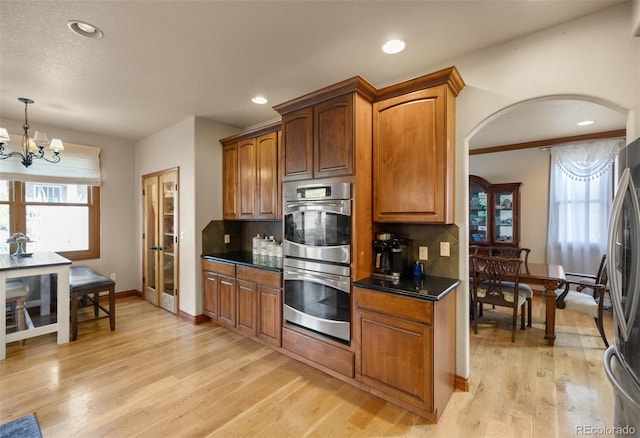 10215 W Wesley Dr, Lakewood, CO 80227 - kitchen with light wood finished floors, appliances with stainless steel finishes, dark countertops, arched walkways, and decorative backsplash