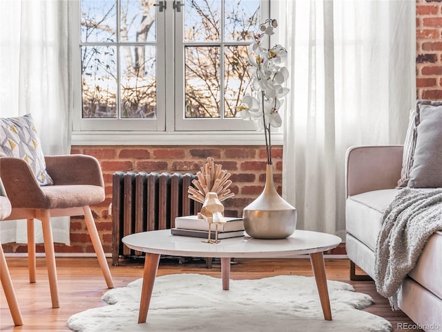 living area featuring radiator, wood-type flooring, a healthy amount of sunlight, and brick wall