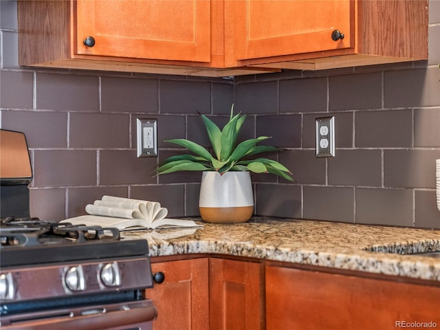 room details with tasteful backsplash, gas stove, and light stone countertops