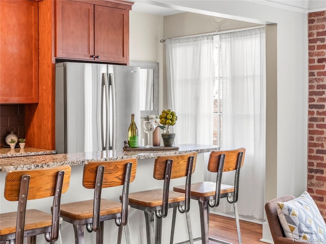 kitchen featuring tasteful backsplash, stainless steel fridge, light stone counters, and light hardwood / wood-style flooring