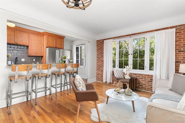 living room featuring brick wall, radiator heating unit, sink, and light hardwood / wood-style floors