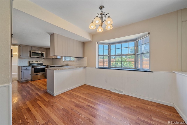 1923 S Newark Way, Aurora, CO 80014 - kitchen with appliances with stainless steel finishes, wood finished floors, backsplash, a chandelier, and a peninsula