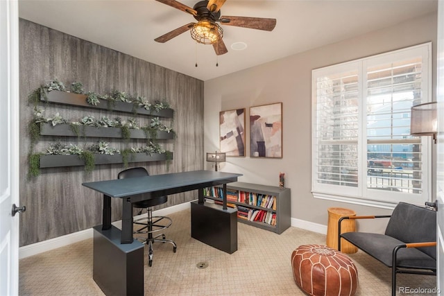 carpeted office with ceiling fan, plenty of natural light, and wooden walls