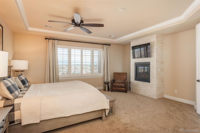 carpeted bedroom with a tray ceiling, a fireplace, visible vents, ornamental molding, and baseboards