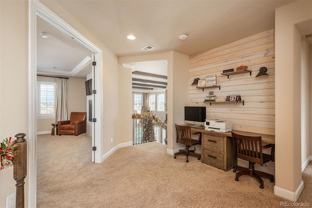 carpeted office with wood walls, baseboards, visible vents, and crown molding