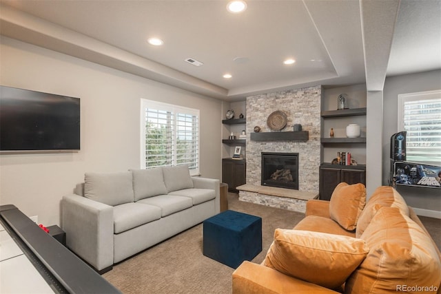 living area featuring built in features, a tray ceiling, recessed lighting, visible vents, and a stone fireplace