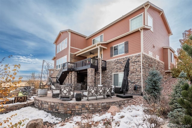 snow covered house with a patio, outdoor lounge area, a ceiling fan, stone siding, and stairs