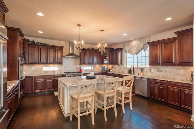 kitchen featuring stainless steel appliances, wall chimney range hood, dark wood-type flooring, and a sink