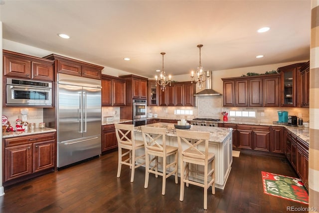 kitchen featuring wall chimney exhaust hood, appliances with stainless steel finishes, dark wood-style flooring, and a center island