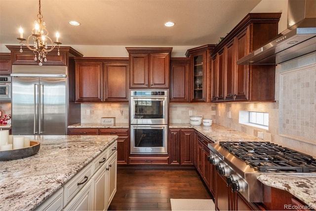 kitchen featuring dark wood finished floors, glass insert cabinets, appliances with stainless steel finishes, light stone counters, and wall chimney range hood