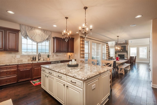 kitchen featuring dark wood-style floors, a center island, a fireplace, tasteful backsplash, and a sink