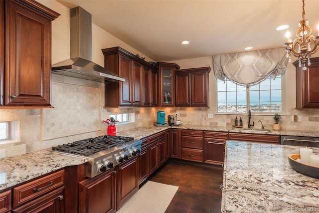 kitchen with light stone counters, appliances with stainless steel finishes, dark wood-style flooring, wall chimney range hood, and a sink