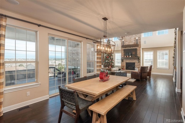 dining space featuring dark wood-style floors, visible vents, a stone fireplace, and baseboards