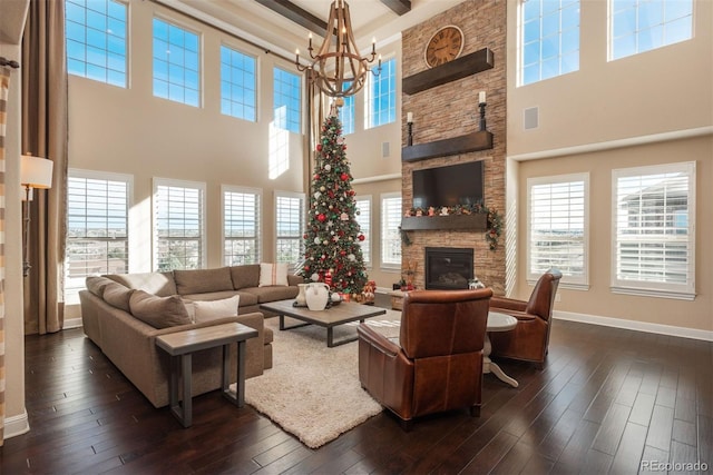 living area featuring dark wood-type flooring, a wealth of natural light, a notable chandelier, and a stone fireplace