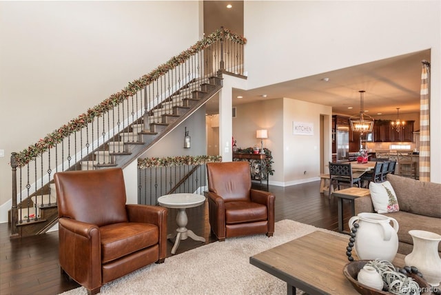 living room featuring a towering ceiling, baseboards, stairs, dark wood-style floors, and an inviting chandelier