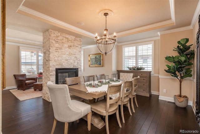 dining area with a stone fireplace, dark wood-type flooring, a raised ceiling, and crown molding