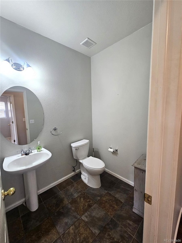 bathroom with stone finish flooring, visible vents, baseboards, and toilet