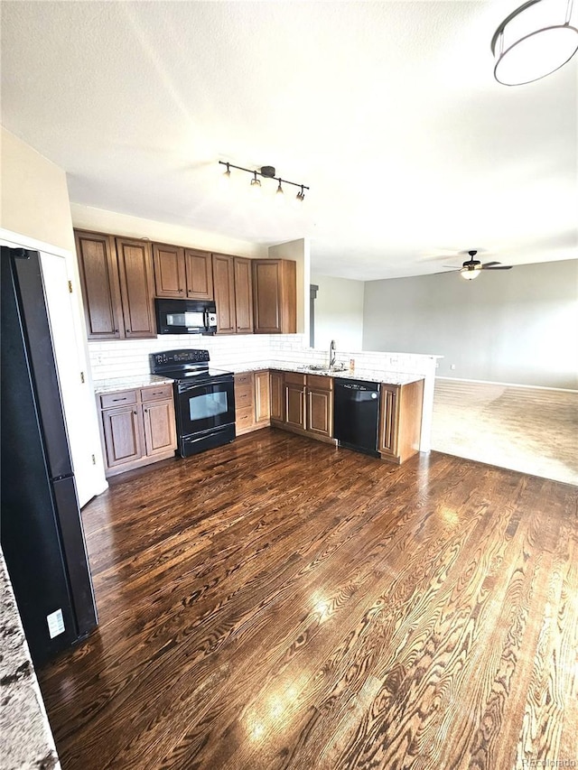 kitchen featuring dark wood finished floors, a peninsula, black appliances, ceiling fan, and a sink