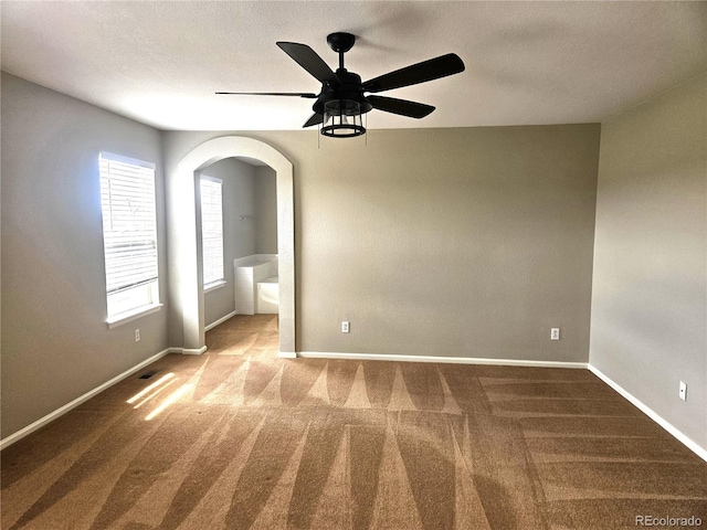 carpeted empty room featuring arched walkways, baseboards, and a ceiling fan