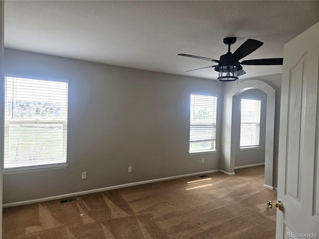 carpeted spare room featuring arched walkways, baseboards, a ceiling fan, and visible vents