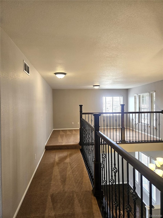 corridor featuring visible vents, baseboards, carpet flooring, and a textured ceiling