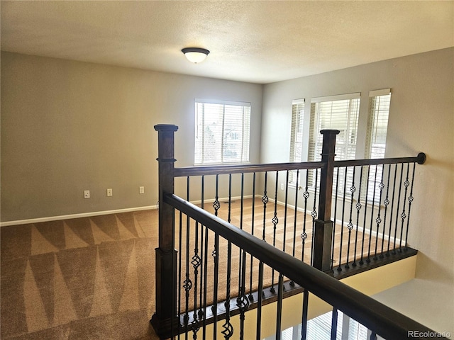 corridor with baseboards, an upstairs landing, carpet, and a textured ceiling