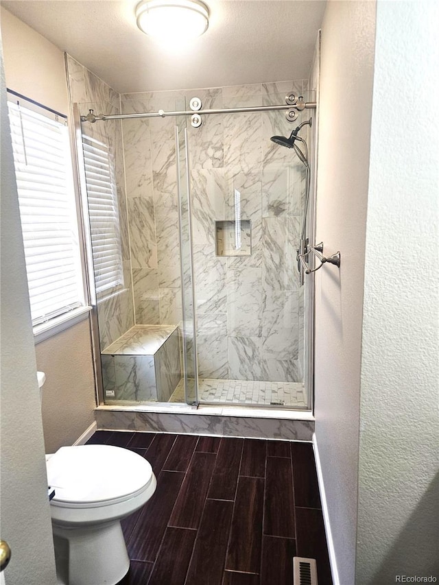 bathroom featuring visible vents, toilet, wood tiled floor, a stall shower, and baseboards