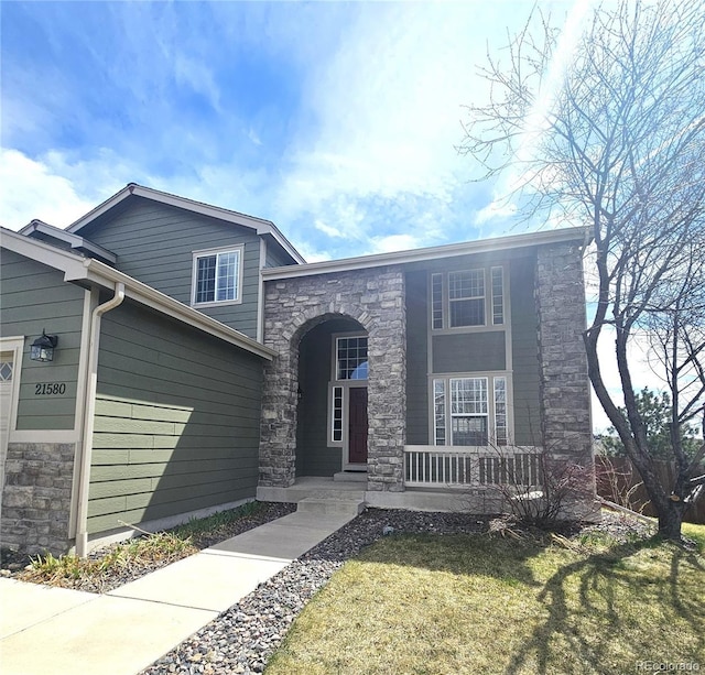 view of front facade featuring stone siding, a front yard, and covered porch