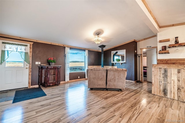 unfurnished living room featuring light wood-type flooring, a wood stove, a wealth of natural light, and ornamental molding