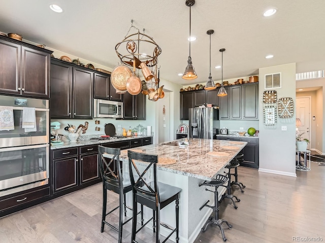 607 Azalea St, Brighton, CO 80601 - kitchen featuring appliances with stainless steel finishes, light wood-style flooring, a breakfast bar area, light stone countertops, and an island with sink