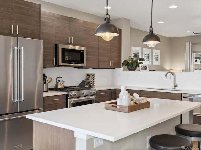 kitchen with a breakfast bar, decorative light fixtures, stainless steel appliances, light countertops, and a sink