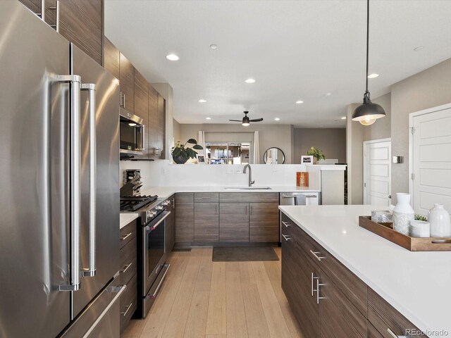 kitchen featuring light wood finished floors, high quality appliances, light countertops, a sink, and recessed lighting