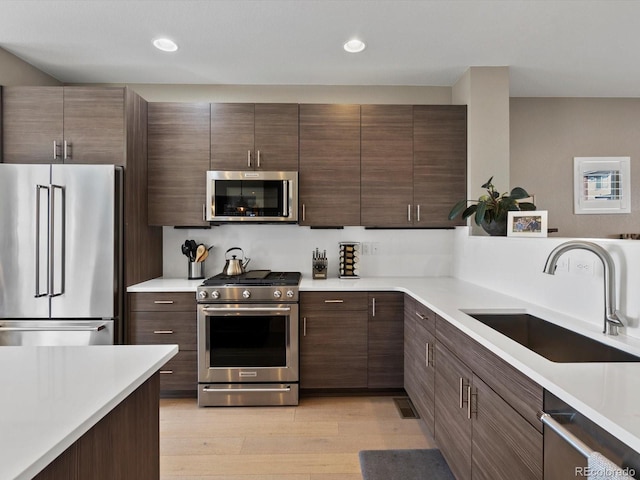 kitchen with stainless steel appliances, recessed lighting, light countertops, light wood-style flooring, and a sink