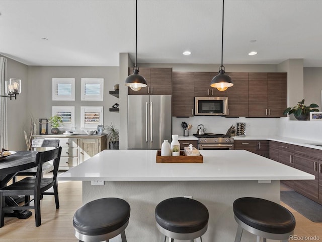 kitchen featuring high quality appliances, a breakfast bar, decorative light fixtures, a center island, and light countertops