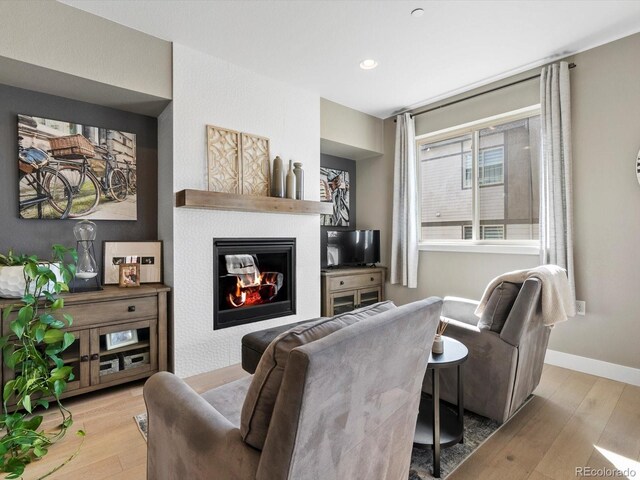 living area with wood-type flooring, baseboards, and a glass covered fireplace