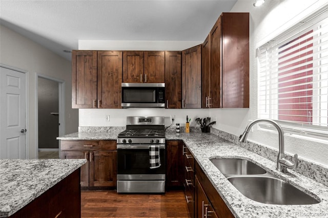 kitchen featuring dark wood-style floors, stainless steel appliances, a sink, and light stone countertops