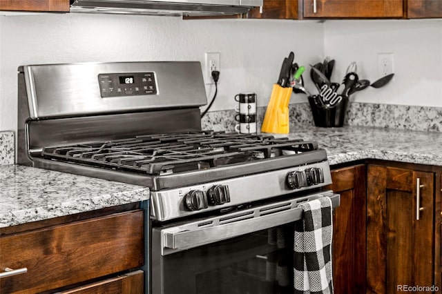 kitchen featuring stainless steel gas range, light stone counters, and dark brown cabinets