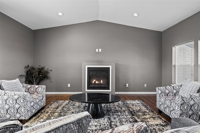 living room featuring vaulted ceiling, wood finished floors, a glass covered fireplace, and baseboards