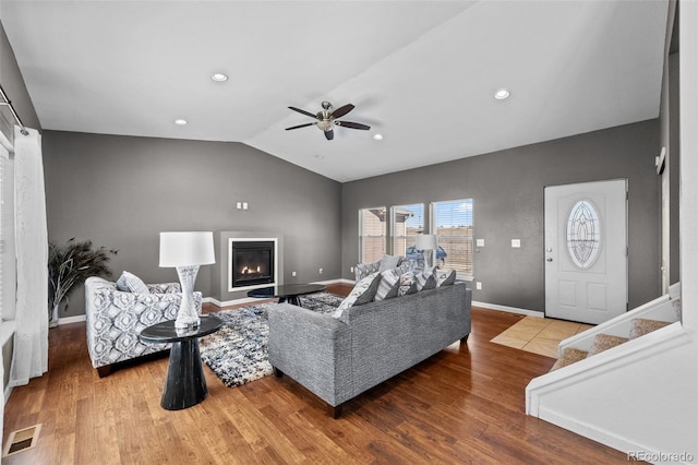 living room with visible vents, a glass covered fireplace, vaulted ceiling, wood finished floors, and baseboards