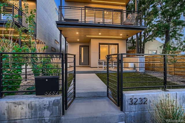 entrance to property featuring a patio, a balcony, fence, and stucco siding