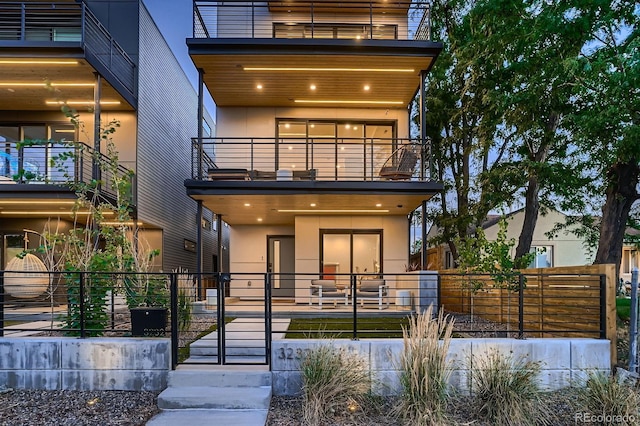 contemporary home featuring stucco siding, a balcony, and fence