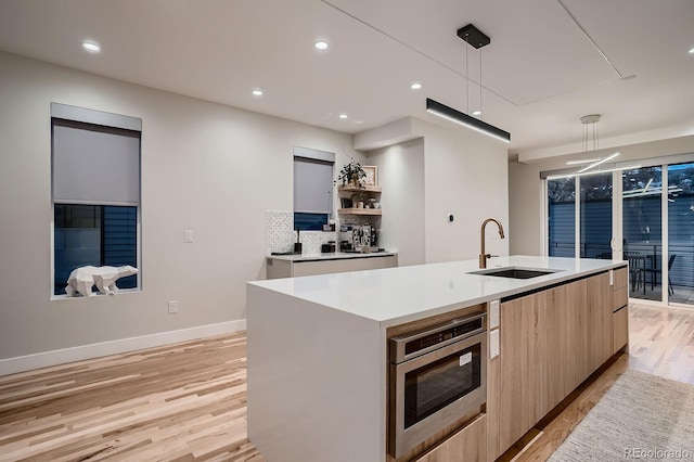 kitchen with modern cabinets, light wood-style flooring, a kitchen island with sink, light brown cabinets, and a sink