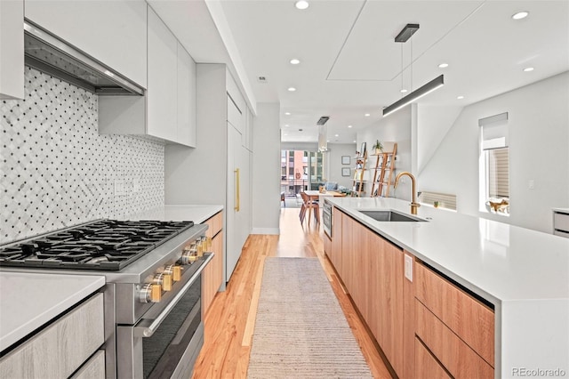 kitchen with a sink, stainless steel stove, light wood-style floors, wall chimney range hood, and modern cabinets