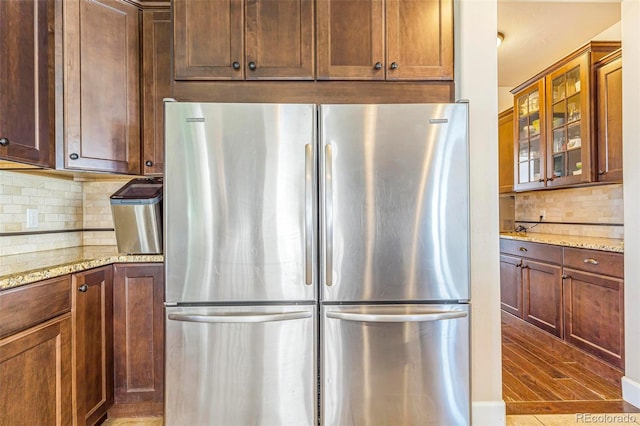 7172 S Oakleaf St, Bennett, CO 80102 - kitchen featuring tasteful backsplash, light stone counters, glass insert cabinets, freestanding refrigerator, and wood finished floors