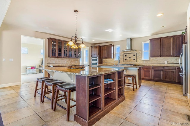 7172 S Oakleaf St, Bennett, CO 80102 - kitchen featuring tasteful backsplash, light tile patterned floors, a kitchen island, wall chimney exhaust hood, and stainless steel appliances