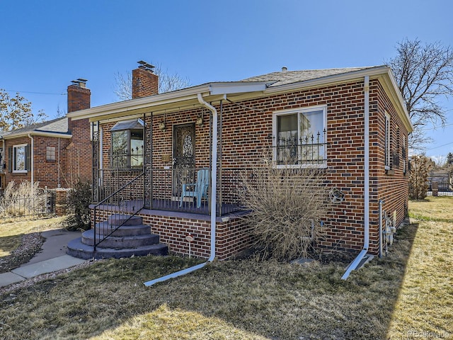 view of front of property featuring a front yard, a chimney, fence, and brick siding