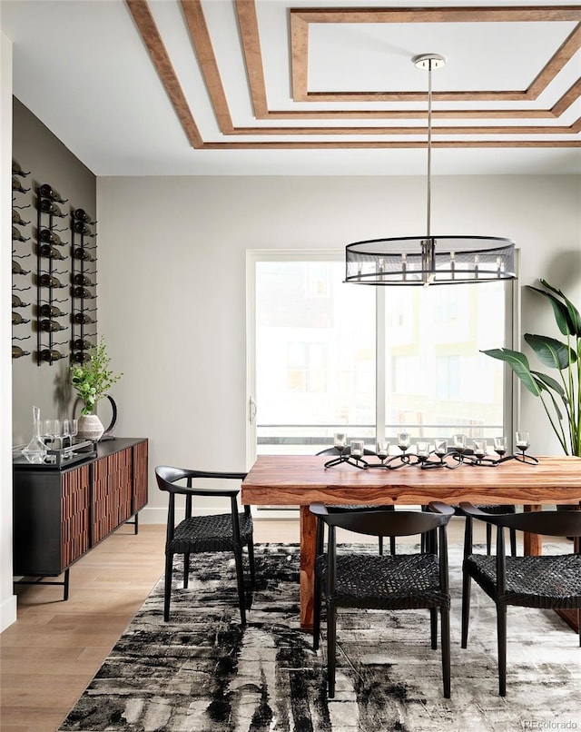 dining area with a raised ceiling, light hardwood / wood-style floors, and an inviting chandelier