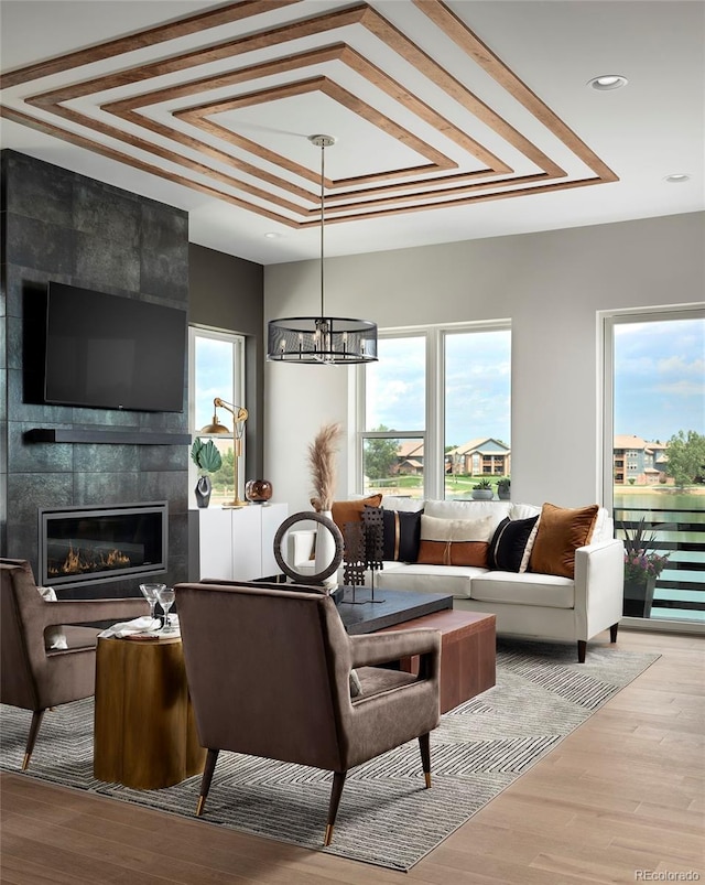 living room featuring light hardwood / wood-style floors, a notable chandelier, a tiled fireplace, tile walls, and a tray ceiling